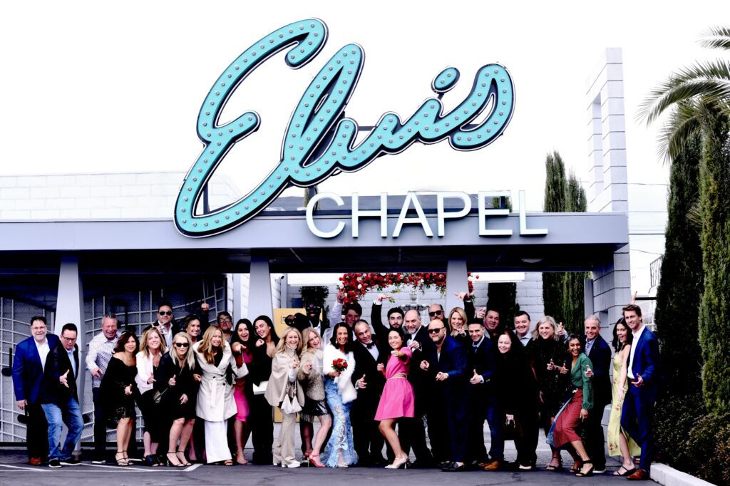 Group celebration outside Elvis Chapel, showcasing a large crowd dressed in formal attire, with a bride holding flowers, highlighting a festive wedding atmosphere.